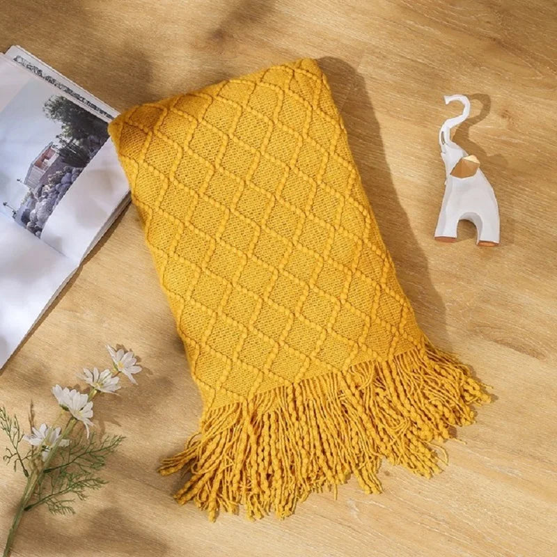 Yellow textured blanket with tassels on a wooden surface with a magazine and decorative item.