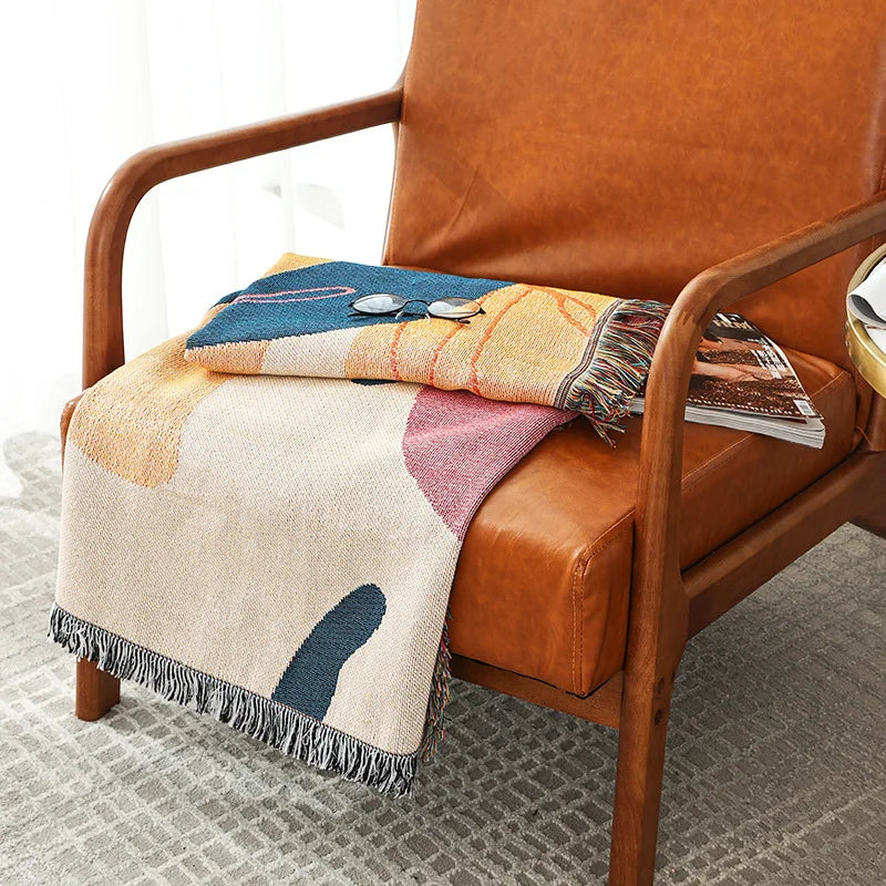 Patterned blanket draped over a brown leather chair with a wooden armrest.