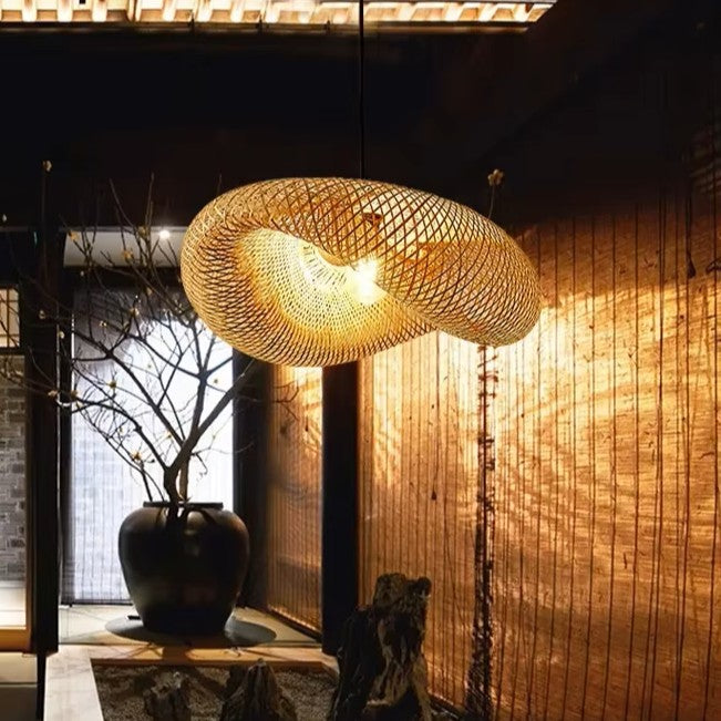 Woven pendant light fixture in a dimly lit room with wooden walls and a potted plant.