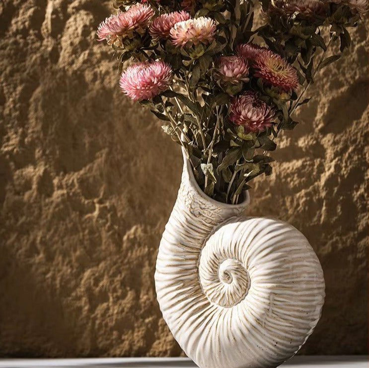 Decorative wall vase shaped like a shell with dried flowers against a textured wall.