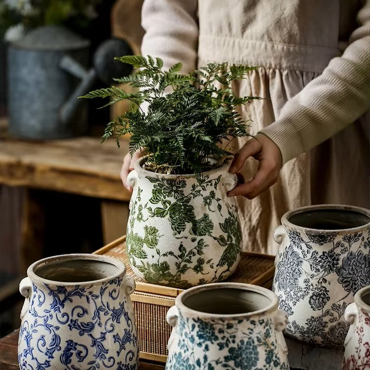 Person holding a potted plant with floral patterns on pots in the foreground