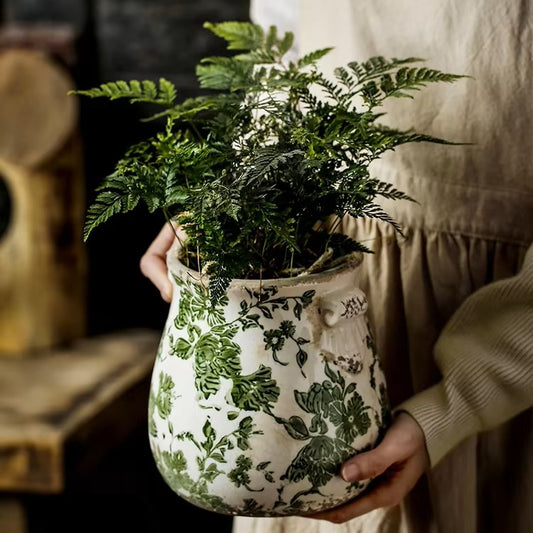 Person holding a potted plant in a decorative pot with floral patterns