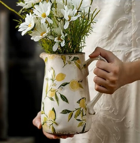 Person holding a ceramic pitcher with floral design filled with flowers