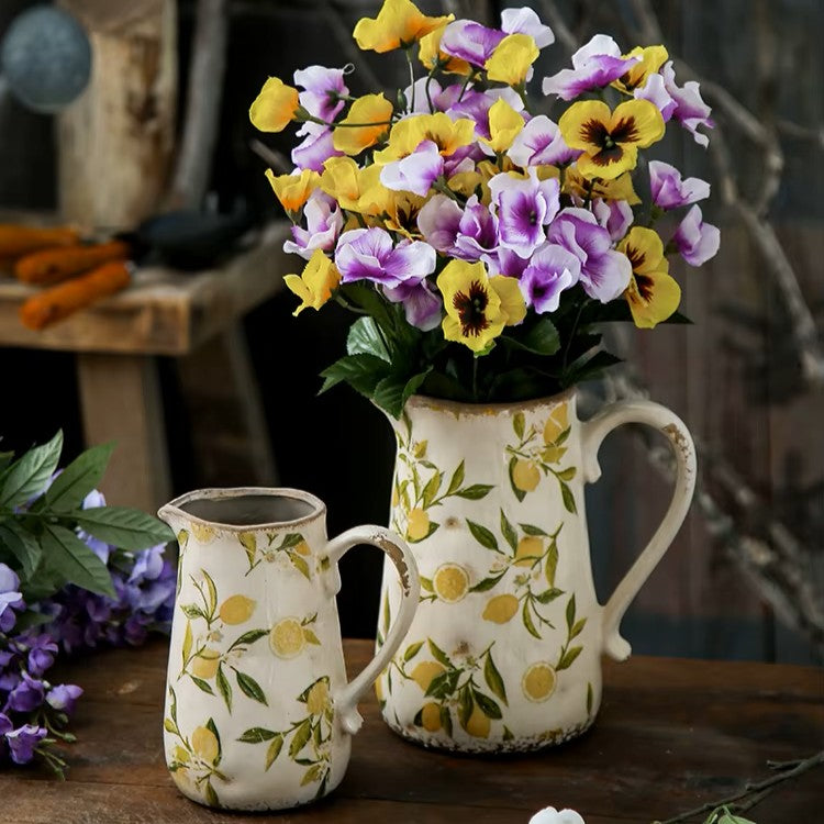 Two decorative pitchers with floral patterns on a wooden surface, one holding a bouquet of yellow and purple flowers.