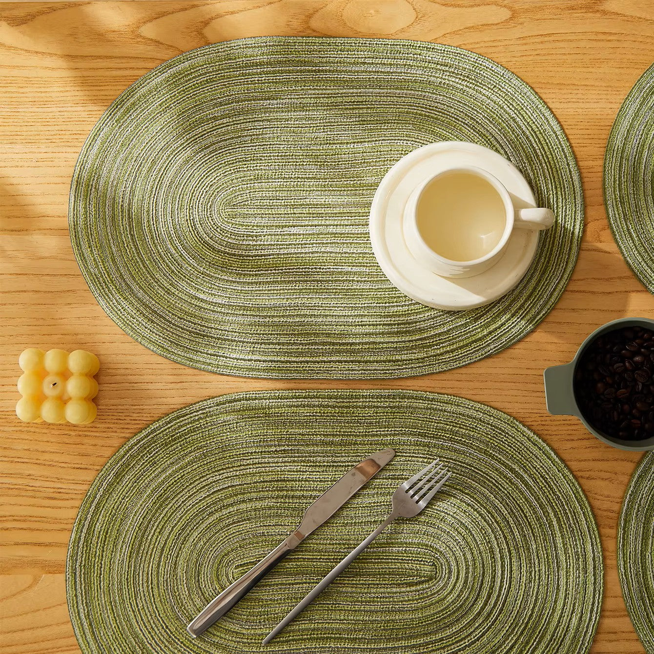 Green woven placemats on a wooden table with cutlery and a cup.