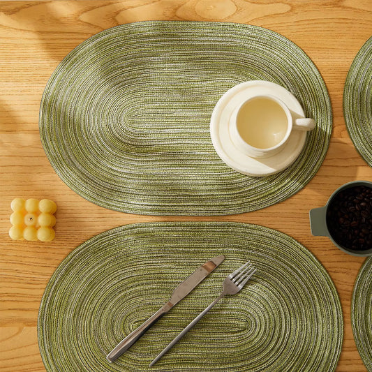 Green woven placemats on a wooden table with cutlery and a cup.