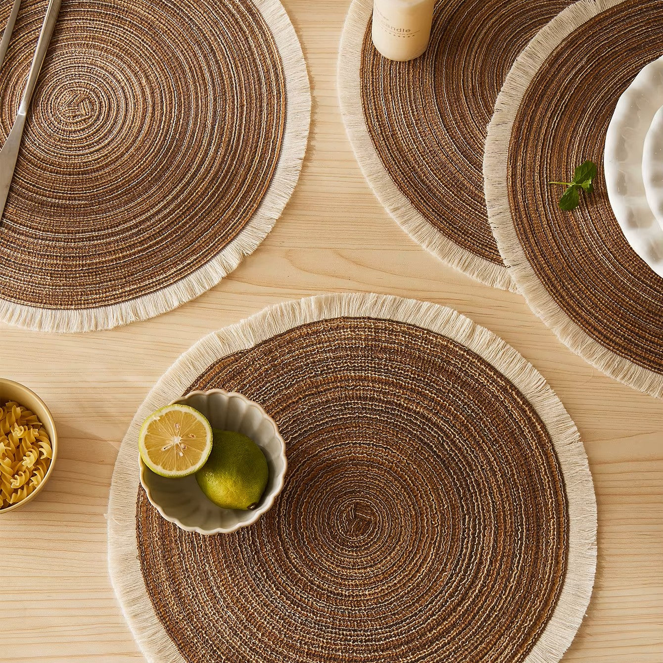 Round woven placemats on a wooden table with a bowl of fruit and a fork.