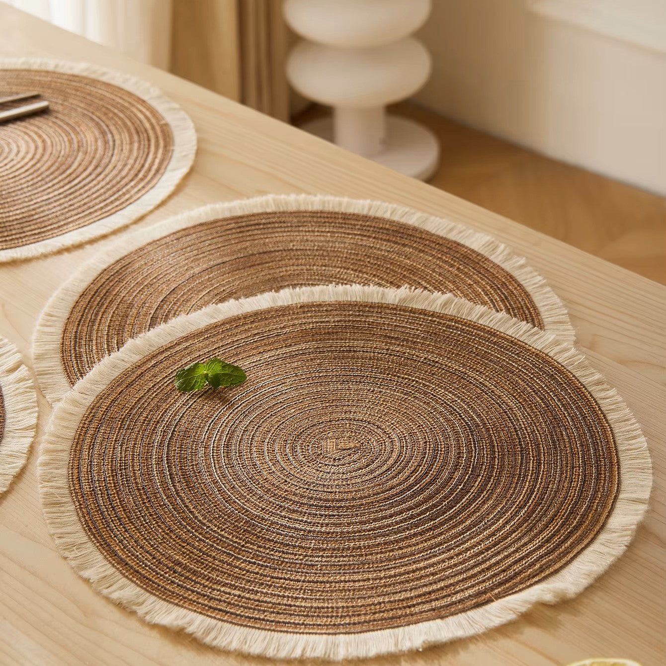 Round woven placemats with tassels on a wooden table.