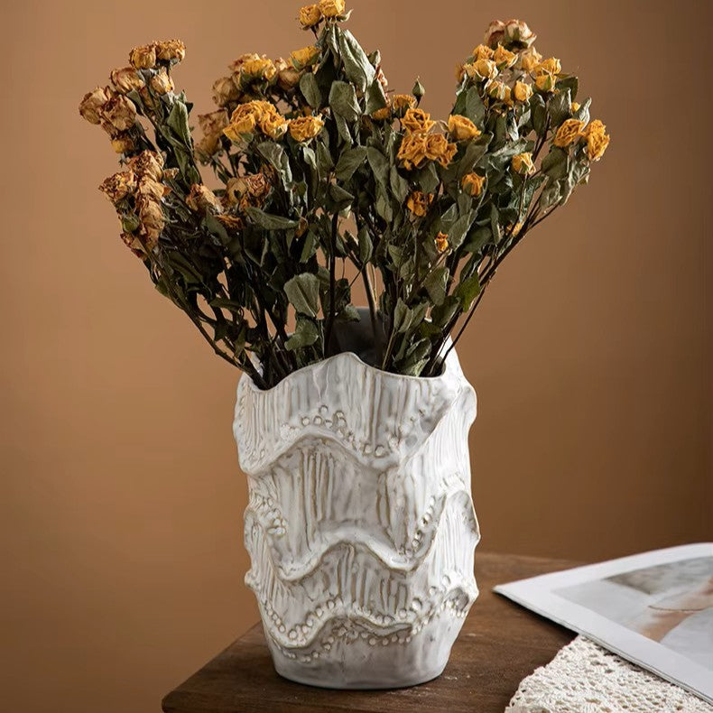 Decorative white vase with textured design holding dried yellow flowers on a wooden surface.