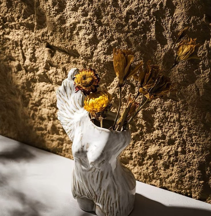 White ceramic vase with dried flowers against a textured stone wall